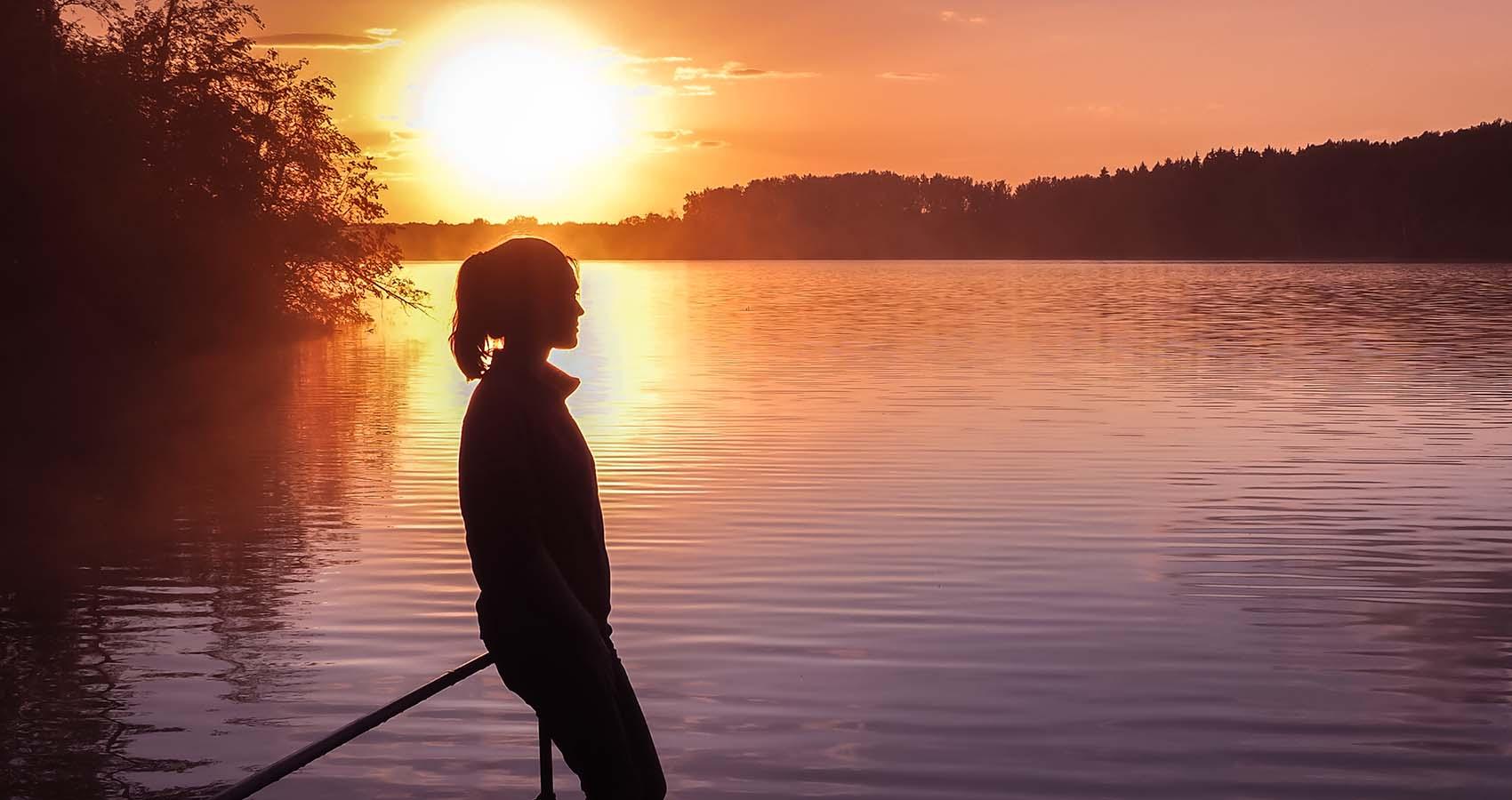 Young teenager overlooking lake at sunset