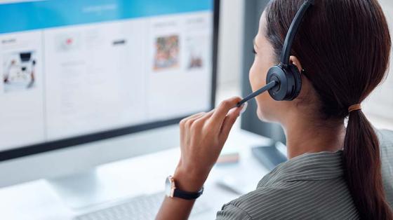 Photo of person taking phone call with a headset and computer
