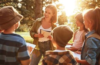 Woman with a notebook talking to a group of kids outside