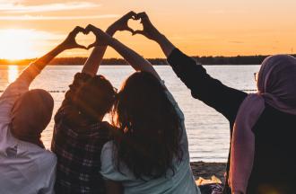 Four people facing water on beach holding hands making heart shapes