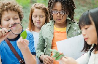 Kids looking at leaf through magnifying glass 