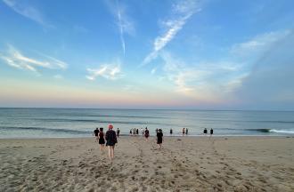 people on sandy beach with blue and orange skyline on the horizon