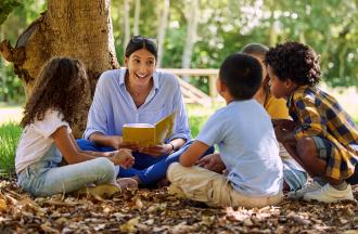 Teacher reading to kids under a tree
