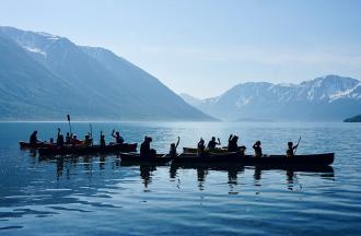 Campers in canoes on lake with mountains in background