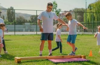 staff helping camper walk across beam