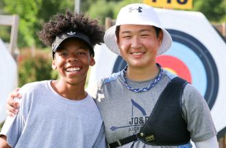 Two smiling young people posing together at an archery range, with colorful circular targets visible in the background