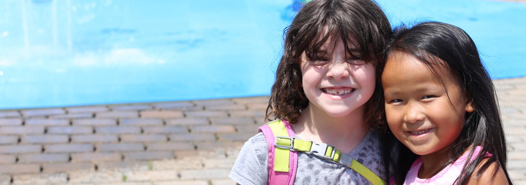 Two young campers smiling while standing in front of pool