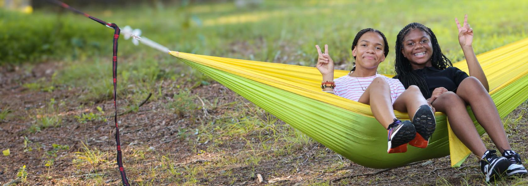 Two campers in hammock holding up peace signs