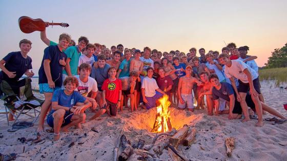 A large group of campers on beach around a campfire