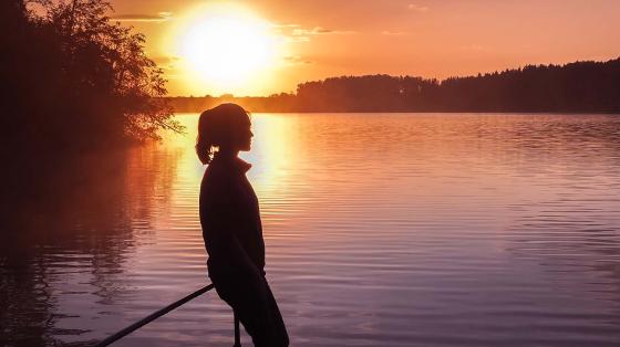 Young teenager overlooking lake at sunset