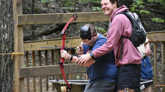 camp staff with camper doing archery