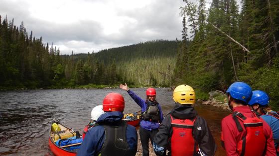 campers wearing helmets and flotation devices standing in front of a body of water