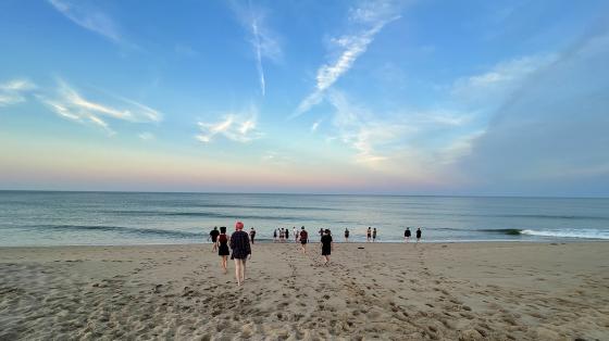 people on sandy beach with blue and orange skyline on the horizon