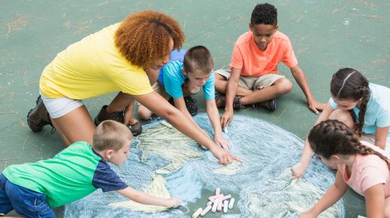 adult helping kids draw with sidewalk chalk