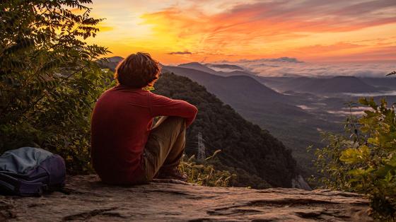 person sitting on rock watching sunset