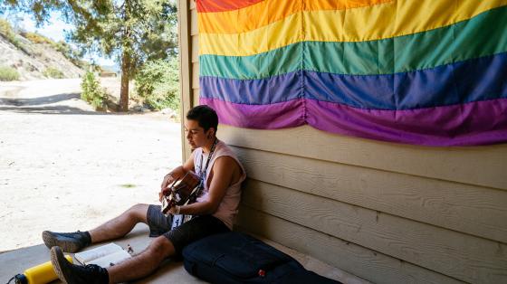 camper playing guitar under rainbow flag