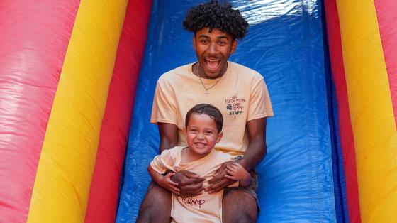 camp staff with camper on inflatable slide
