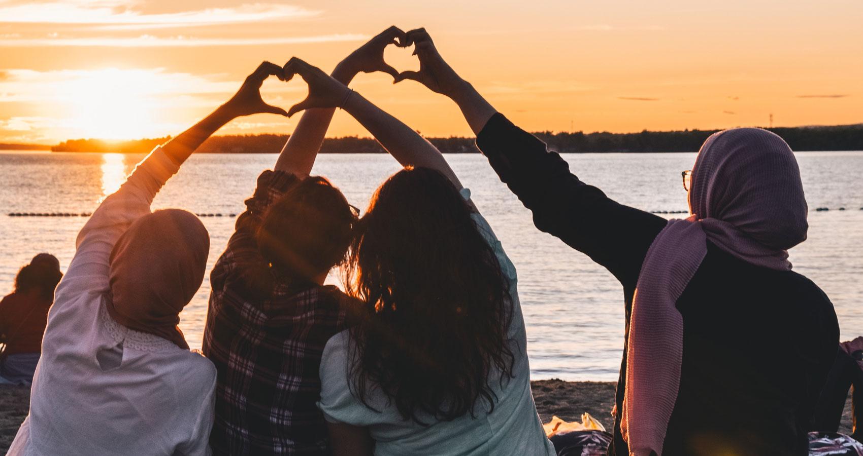 Four people facing water on beach holding hands making heart shapes