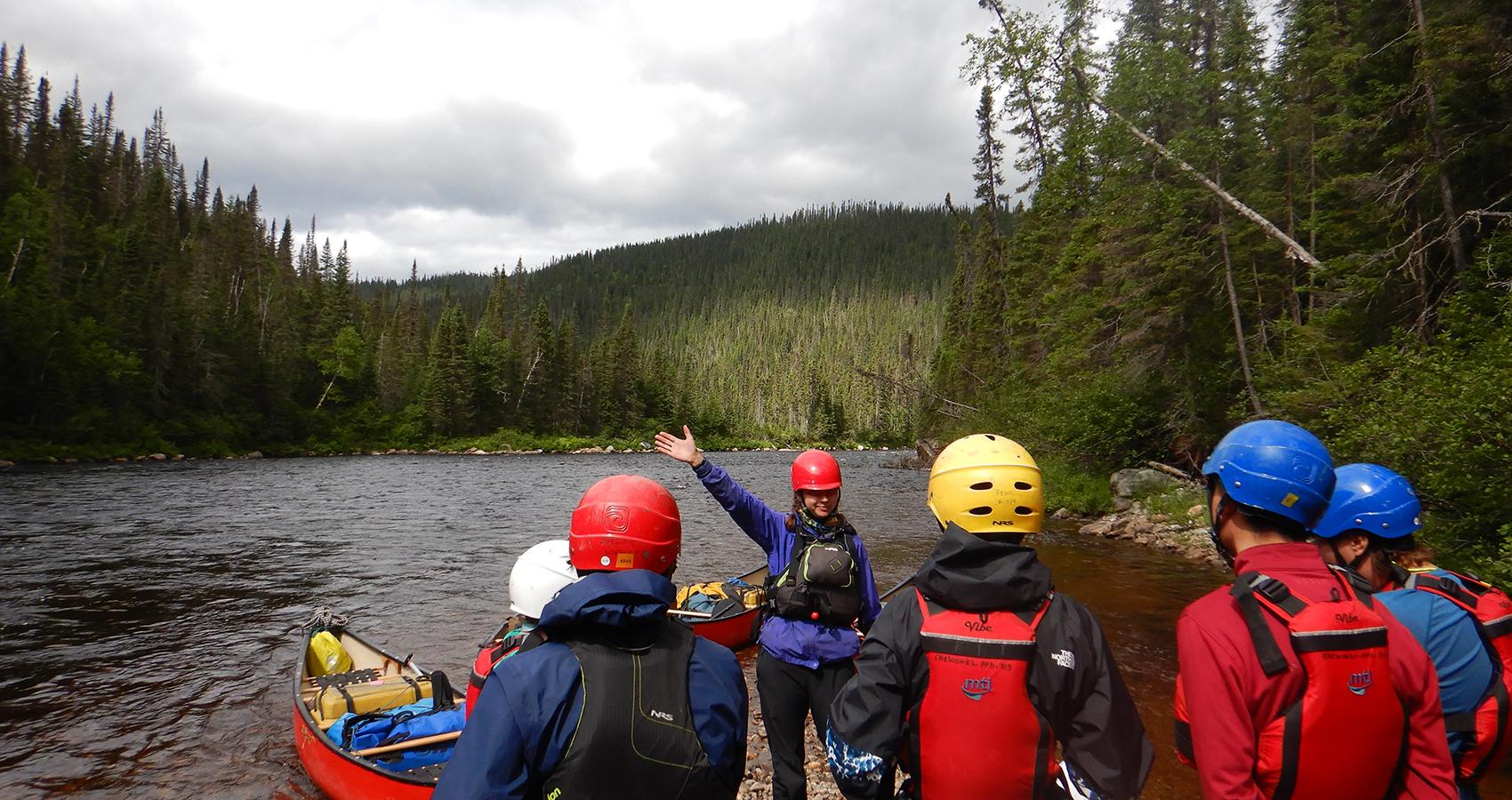 campers wearing helmets and flotation devices standing in front of a body of water