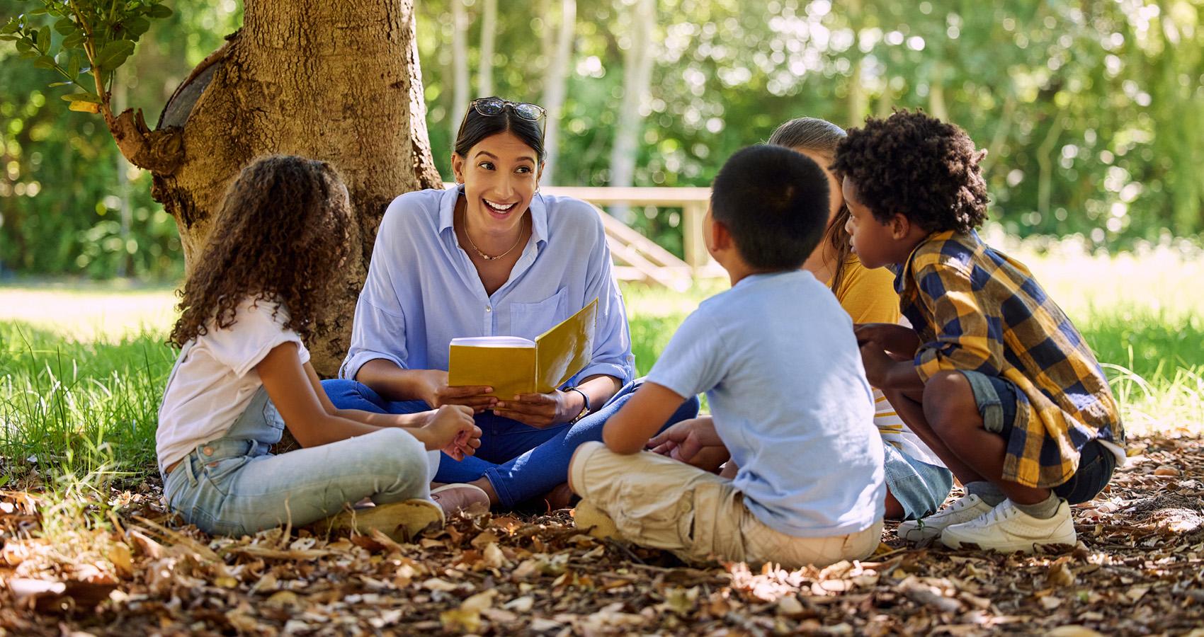 Teacher reading to kids under a tree