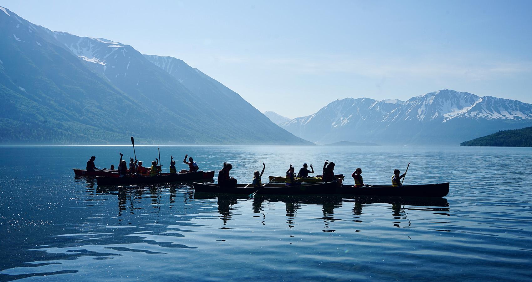 Campers in canoes on lake with mountains in background