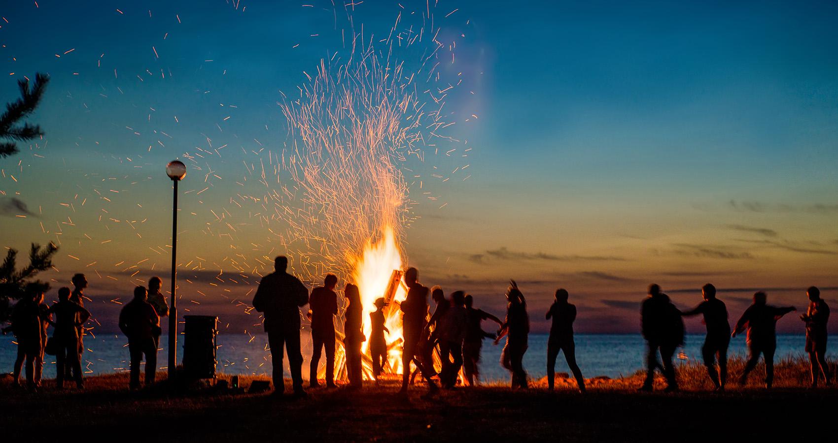Group of people hanging around campfire at sunset