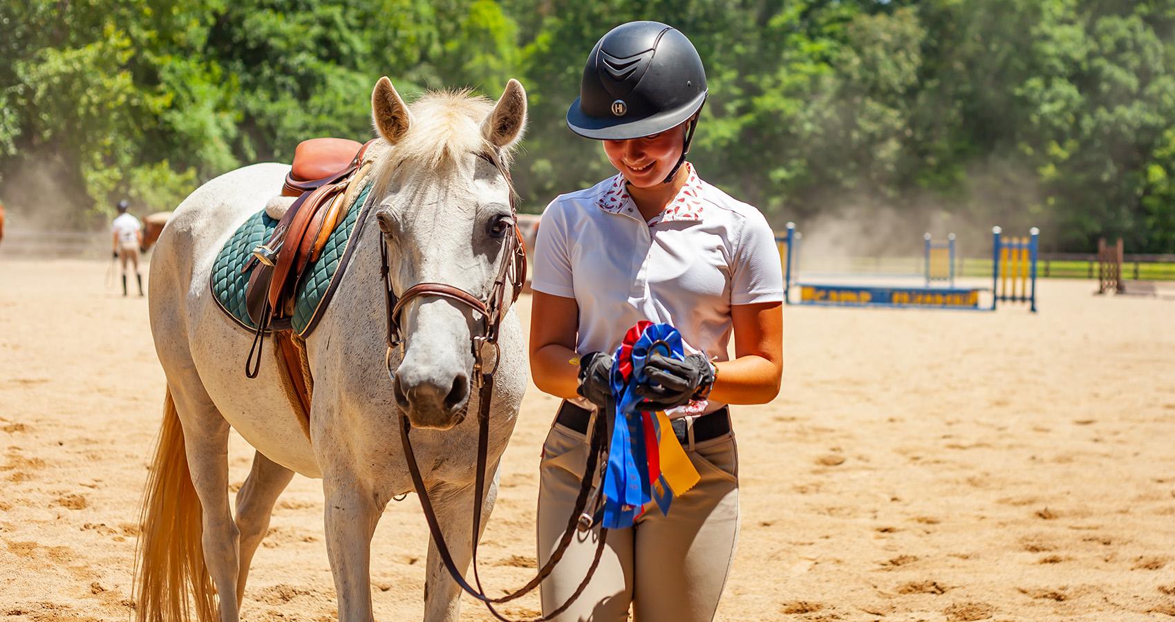 helmeted person holding ribbons standing with horse