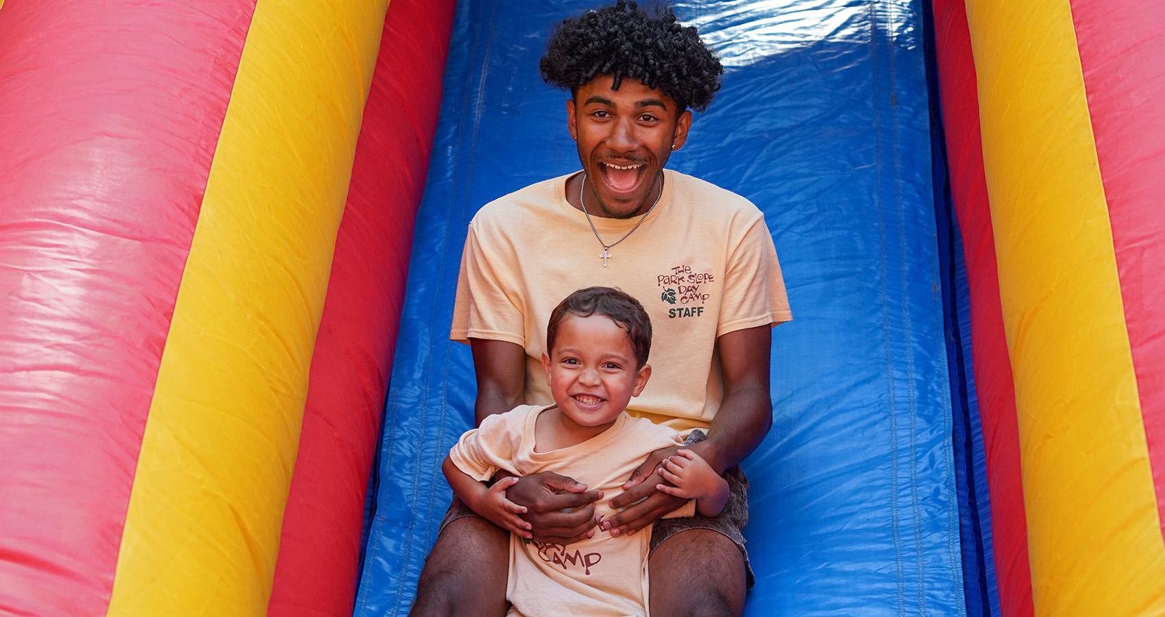 camp staff with camper on inflatable slide