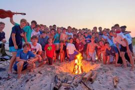 A large group of campers on beach around a campfire