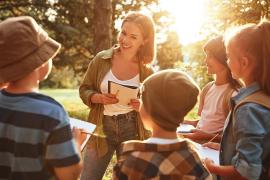 Woman with a notebook talking to a group of kids outside