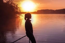 Young teenager overlooking lake at sunset