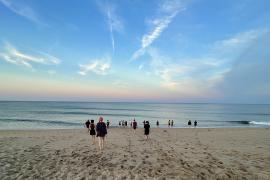 people on sandy beach with blue and orange skyline on the horizon